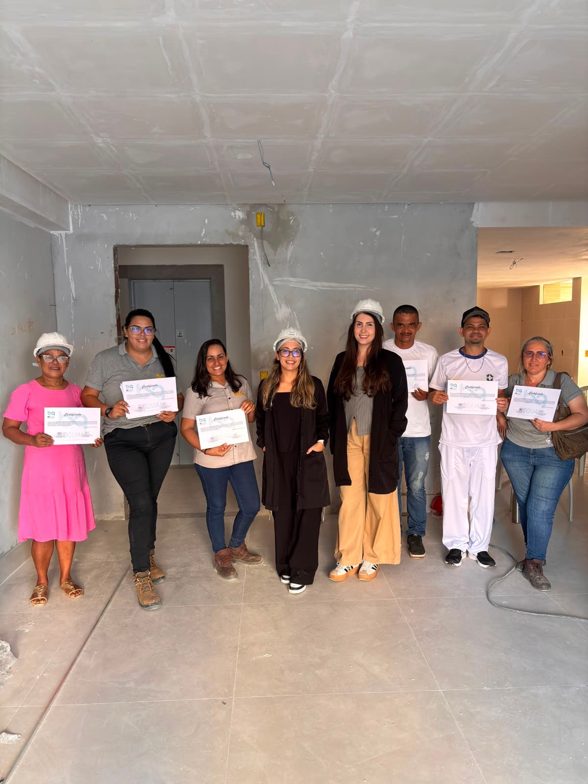 Equipe de cozinha de obra com os certificados de treinamento, em canteiro ainda em acabamento, parte do grupo usando capacete