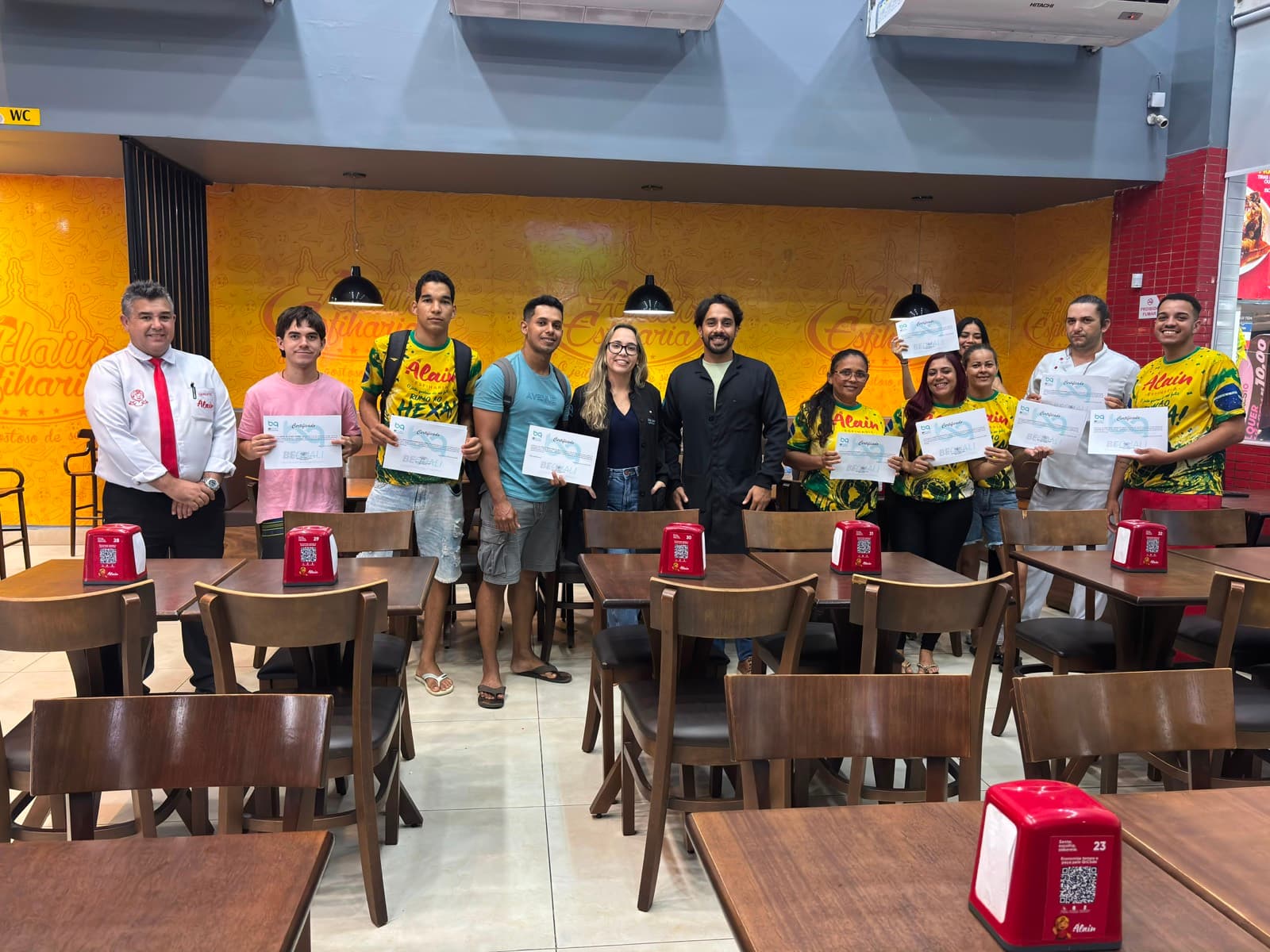 Equipe de restaurante com os certificados de treinamento no salão, ao lado do gerente e das consultoras